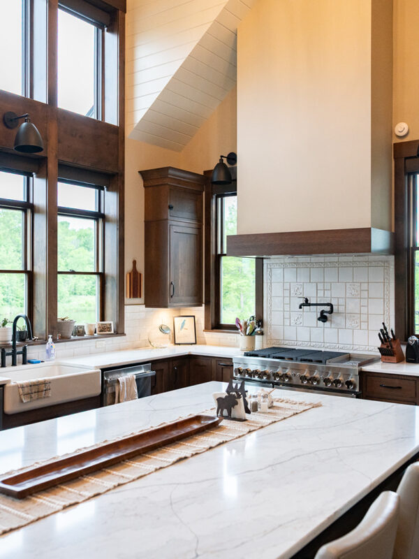 Creative Design Projects project example by Custom Pro Homes. A clean, bright kitchen with white countertops and tiled backdrops, dark wood window frames, and a modern sink with black faucets.